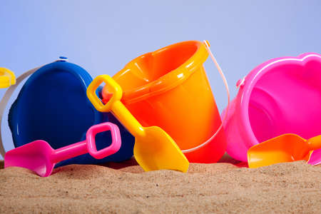 a row of colorful beach buckets or pails with shovels on a sandy beach with blue sky background with copy spaceの写真素材