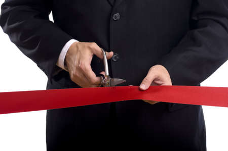 A man in a business suit cutting a red silk ribbon with shiny scissors, grand opening or beginning conceptの写真素材