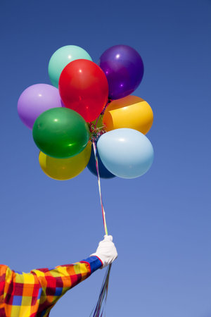 A clown holding a group of colorful balloons in front of a blue sky