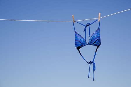 a blue bikini swimsuit top hanging on a clothesline in front of a cloudless blue skyの写真素材