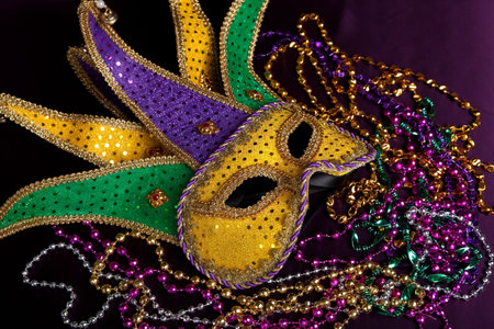 glittery gold, green and purple mardi gra mask with beads on a purple background の写真素材