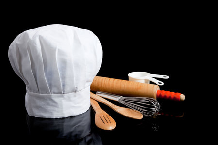 A white toque with cooking utensils including rolling pin, wooden spoons, wisk and measuring cups on...