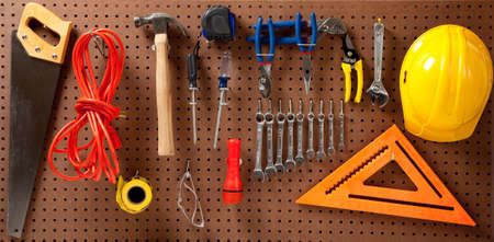 Peg board with hardhat, extension cord, flashlight, hammer, screw driver, caution tape, carpenter's square and pliersの写真素材