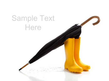 A pair of yellow rainboots and a black umbrella on a white background with copy spaceの写真素材