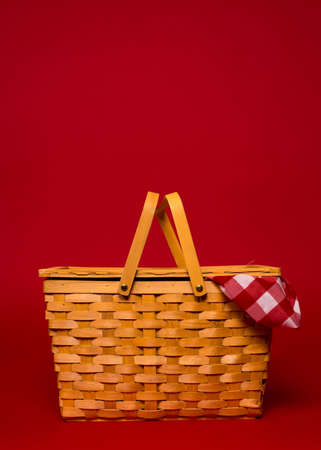 A brown, wicker picnic basket with red gingham tablecloth on a red with copy spaceの写真素材