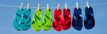 Turquoise, green, red and blue flipflops on a clothesline with the sky in the の写真素材