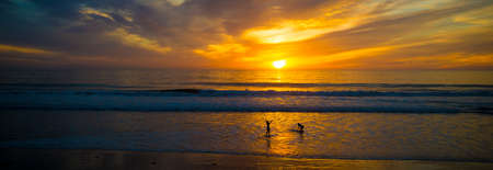 Beautiful Sunset on the ocean with silhouettes of surfersの写真素材