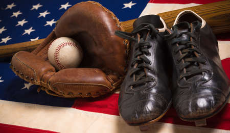 An old, antique American flag with vintage baseball equipment on a wooden benchの写真素材