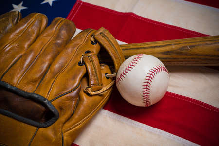 An old, antique American flag with vintage baseball equipment on a wooden benchの写真素材