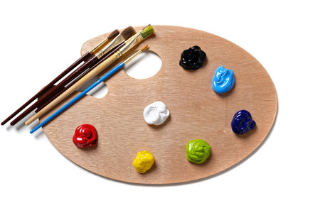 A wooden artists or painters palette with unused, bright colored paint and brushes on white...