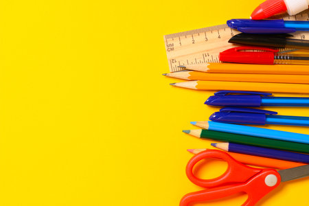 Assorted school supplies, including pencils, pens, scissors and a wooden ruler on a yellow...