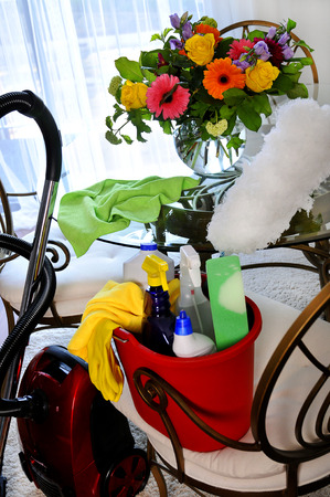 Bucket with cleaning supplies and vacuum cleaner, on table vase of flowersの写真素材