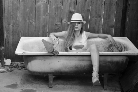 Black and white photo of beautiful, sexy blonde cowgirl in western style in a bathの写真素材