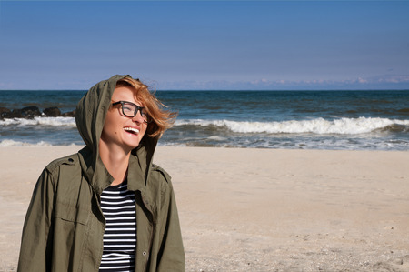 Happy woman in warm clothes jacket on the beach against the ocean in the cold season enjoying a walking by the beach sea in autumnの写真素材