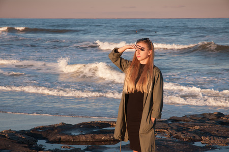 Beautiful view of ocean, woman looking at the sea during the sunset on the beach in autumnの写真素材