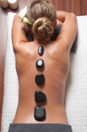 Beauty treatments woman getting spa on a stone therapy, hot stone massage. Girl resting at spa salon on vacationの写真素材