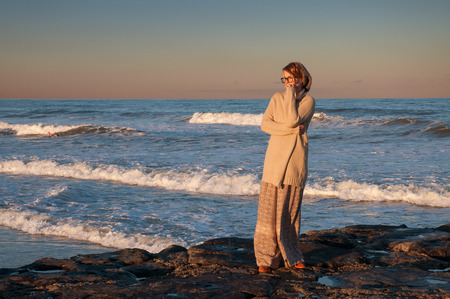 Beautiful view of ocean, woman looking at the sea during the sunset on the beach in autumnの写真素材