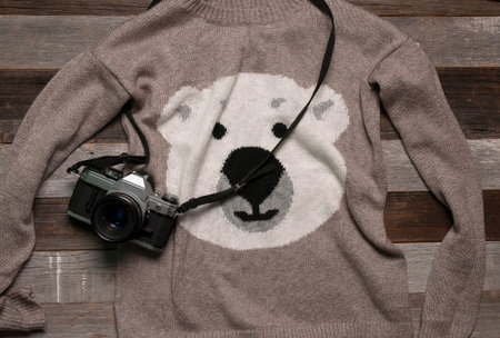 Winter clothes knitted warm sweater and camera on a wooden table


