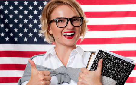 Smiling young woman on United States flag background. Student is learning English as a foreign language. American flag.の写真素材