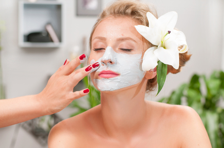Beauty treatment and spa salon. Beautiful woman applying clay facial mask at beauty salonの写真素材