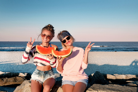 Happy girls eating watermelon on the beach. Friendship, happiness, joy, beach, summer concept. Young people having fun on the beach.の写真素材