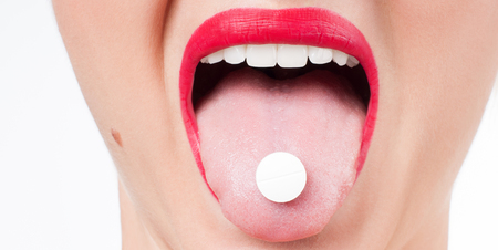 Open mouth holding medicine pill on tongue.  Woman  with red lips taking medicine.の写真素材