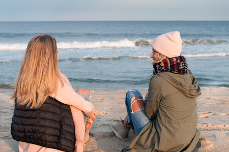 Friends. Back view of two girls looking at sea on the beach in autumn.の写真素材