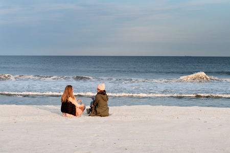 Friends. Back view of two girls looking at sea on the beach in autumn.の写真素材
