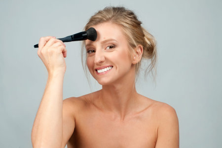 Beauty. Makeup. Beautiful woman applying dry cosmetic tonal foundation on the face using makeup brush.の写真素材