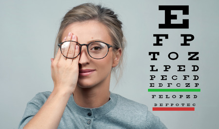Woman in glasses reviewing eyesight closing eye with hand. Eye test. Eyesight vision exam chartの写真素材