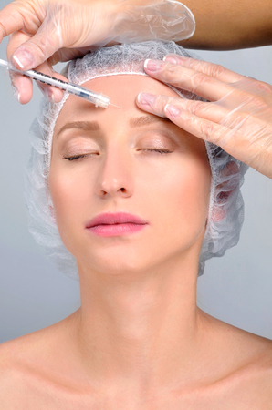 Woman is getting filler injection in forehead. Anti-aging treatment and face lift. Cosmetic Treatment. Facial skin lifting injection to woman's face. Plastic Surgeryの写真素材