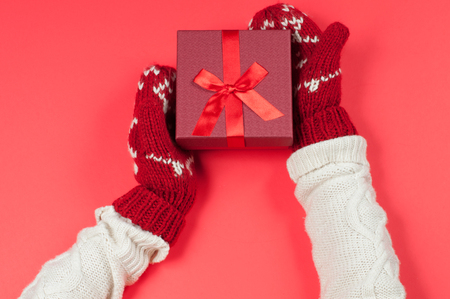 Female hands holding christmas gift box in red mittensの写真素材