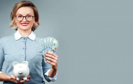 Woman holding piggy bank and bunch of money banknotes. Financial budget savings, smart investment conceptの写真素材