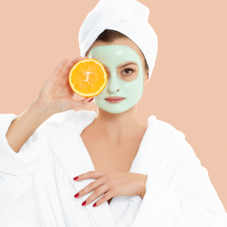 Beautiful woman is getting facial clay mask on pastel background. Beauty, body care and spa conceptの写真素材
