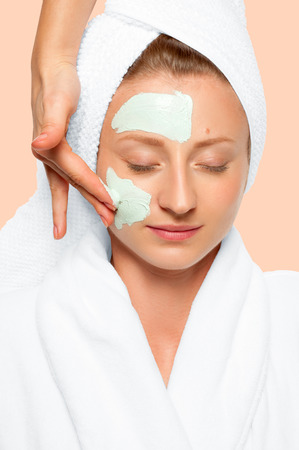 Treatment in spa salon. Beautiful young woman with cosmetic clay mask on face. Faded pastel colorの写真素材