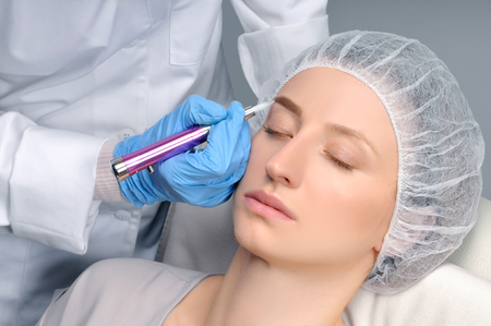 Microblading eyebrows. Cosmetologist making permanent makeup. Attractive woman getting facial care and tattoo at beauty salonの写真素材