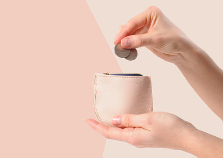 Female hands is putting coins in wallet on pastel faded background