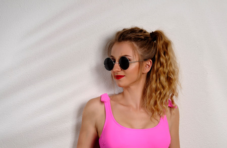 Beautiful woman wear pink swinsuit and sunglasses on white wall with shadow of palm leavesの写真素材