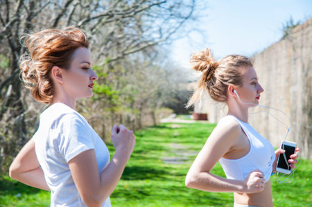 Happy sporty women running and listening to music. Female fitness training outside.の写真素材