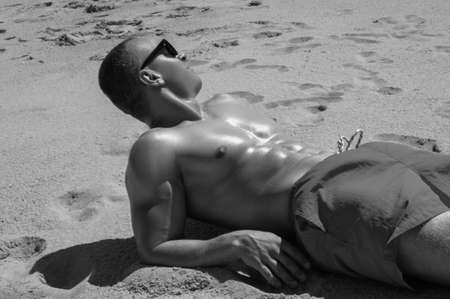 Muscular young athletic sexy man lying on the beach with a naked torsoの写真素材