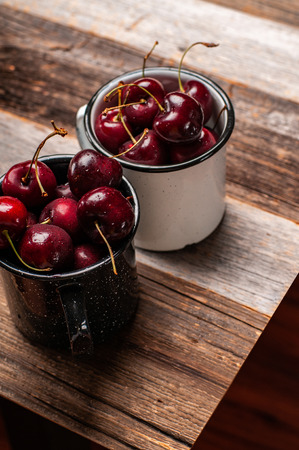 Fresh ripe cherries. Cherries in the enameled cup on wooden tableの写真素材