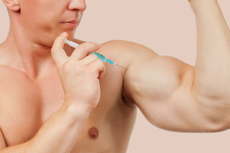 Bodybuilder taking steroids injection in arm on pastel background.の写真素材