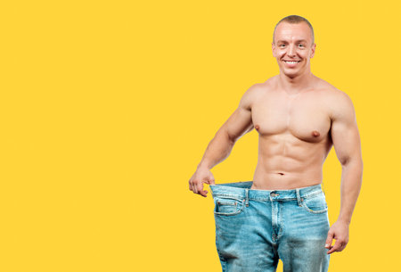 Man wearing big jeans after diet, weight loss concept on yellow background