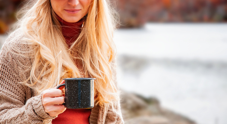 Woman holding cup of tea in the hands outdoor. Beautiful woman drinking hot tea in autumn forest.の写真素材
