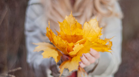 Beautiful woman is holding yellow leaves in autumn forest enjoying nature.
