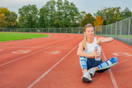 Fitness woman in sport clothes holding bottle of water outdoor on running trackの写真素材