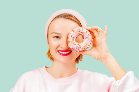 Portrait of happy woman with colorful donut against her eyes on pastel green backgroundの写真素材