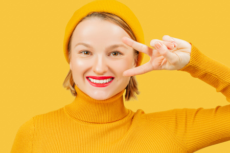 Young beautiful woman on yellow background smiling with happy face showing victory sign. の写真素材