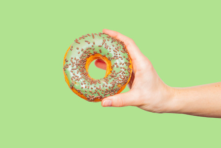 Female hand holding donut. Colorful donut on pastel green backgroundの写真素材