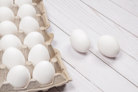 Raw chicken eggs in egg box on white wood background